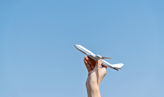 Woman hand holding model airplane under blue sky.