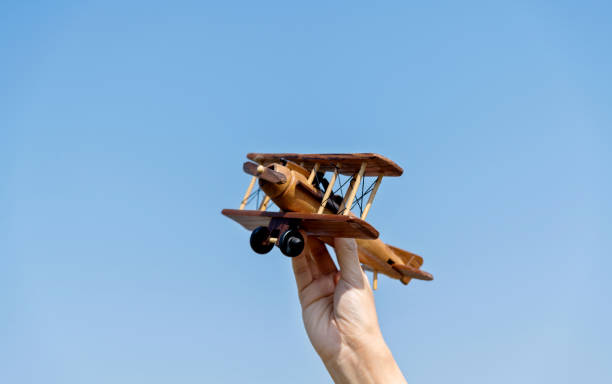 Interior cockpit view of a yellow vintage biplane showing the wooden instrument panel with gauges, control details, and supporting struts. The angle looks upward toward the fabric-covered wing, with sunlight highlighting the textures against a bright blue sky.