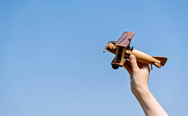 Woman hand holding model airplane under blue sky.