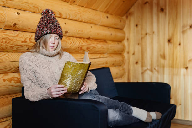 dorosła kobieta relaksująca się na przytulnej kanapie w domku z bali w mroźną zimę. - home interior luxury book chalet zdjęcia i obrazy z banku zdjęć