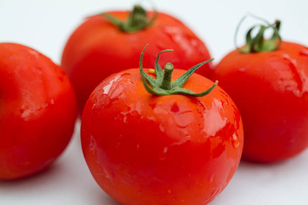 details einer roten tomate mit grünem stipe und anderen verschwommenen tomaten im hintergrund - caulis stock-fotos und bilder