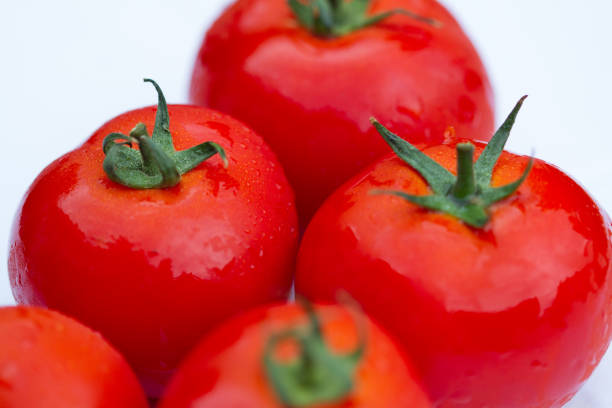 details einer roten tomate mit grünem stipe und anderen verschwommenen tomaten im hintergrund - caulis stock-fotos und bilder