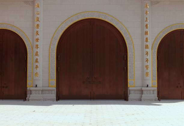 decorative stained red wood gate. carved ornate panels. urban setting with beige stucco finished framed opening. circular columns on square stone base. cobble stone street paving. architecture