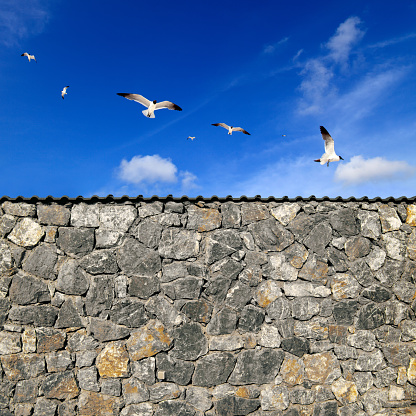 Close up stone wall over sunny blue sky with group of flying seagulls