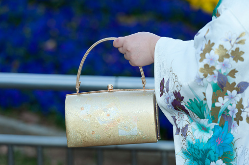 Beautiful Japanese teenager wearing traditional kimono close-up on handbag celebrating the Coming of Age Day in Fuji City, Japan. Background with defocused blue flowers.