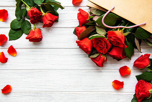 Frame made of red roses, petals   on white wooden background. Flat lay, top view, copy space.