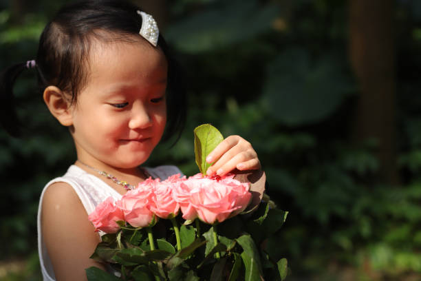a smiling Asian girl holding rose flowers in a forest.