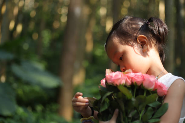 a smiling Asian girl holding rose flowers in a forest.