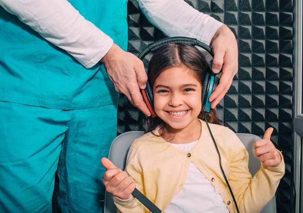 criança misturada positiva da raça que desgasta os auscultadores que mostram polegares acima ao testar do exam.audiometry da audição - hearing aid audiologist audiology small - fotografias e filmes do acervo