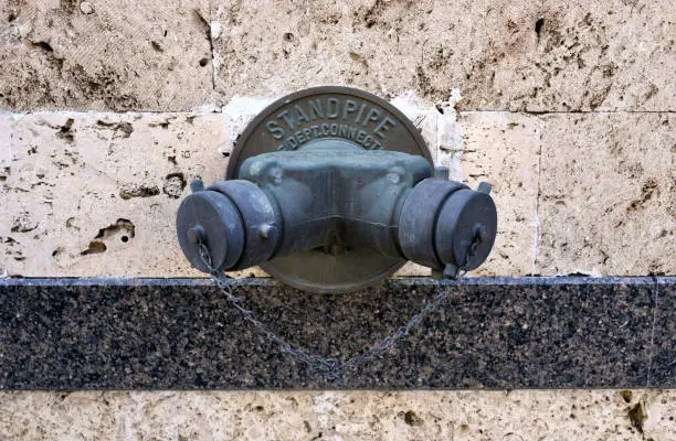 Wall mounted standpipe hydrant system for fire fighting - sign reads "fire department connections" - coral rock wall.