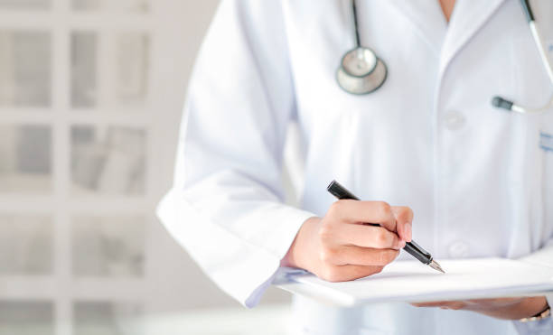 istock Cropped image of doctor hand writing on application form while standing at hospital. Copy space. 1193893379