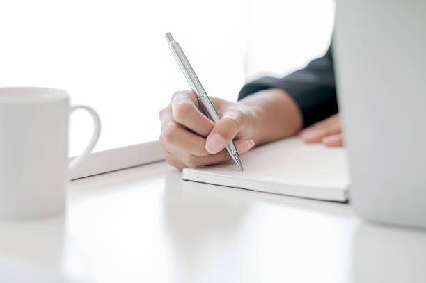 istock Cropped shot of female hand using pen writing on blank notebook while sitting at office desk. 1193897897