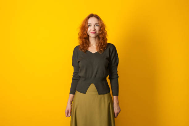 Studio portrait of a 45 year old red-haired woman Studio portrait of an attractive red-haired 45 year old woman in a green sweater on a yellow background mature skirt pictures stock pictures, royalty-free photos & images