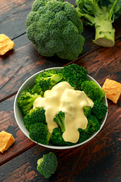 Broccoli with cheese sauce in white bowl on wooden table