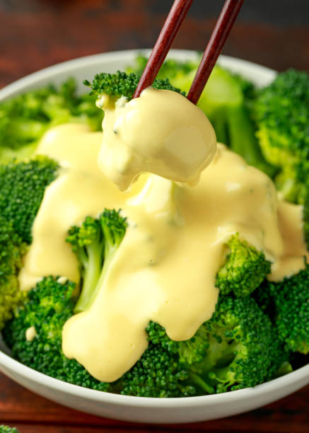 Broccoli with cheese sauce in white bowl on wooden table