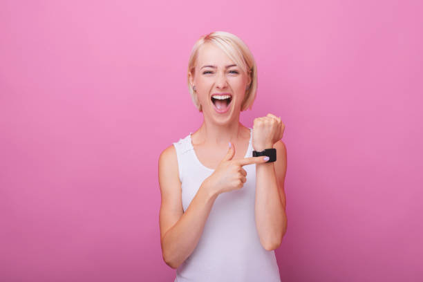 photo of excited blonde woman, pointing at her watch, standing over pink isolated background - clock face clock deadline human hand imagens e fotografias de stock