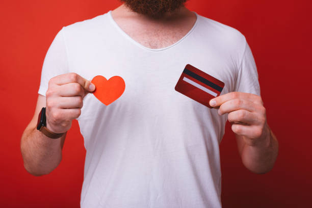 I love credit cards and paying online. Man holding a red credit card and a heart shaped paper on red background. stock photo