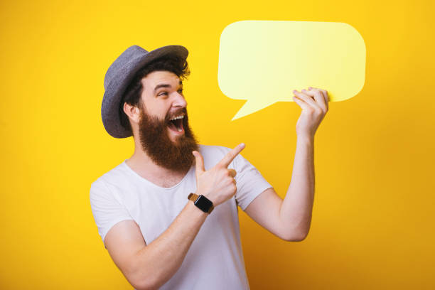 istock Look at this! Excited bearded man pointing at a speech bubble he is holding. Yellow theme. 1193903442