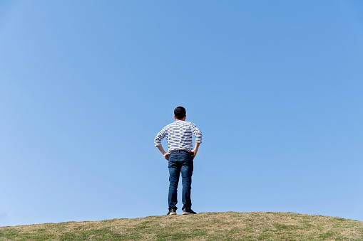 Man standing on meadow with arms akimbo.