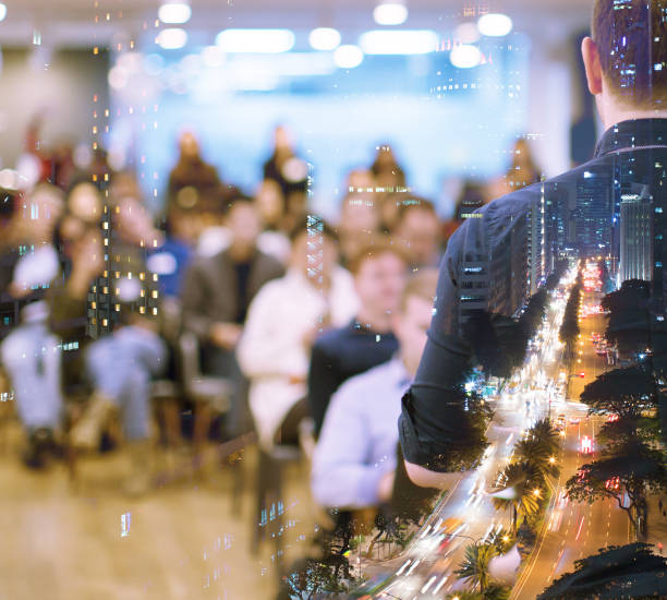 istock Conference photo audience and speaker giving speech. Seminar presenter during forum. Manager in executive training presentation on stage. Double exposure with business background and city. 1193908906