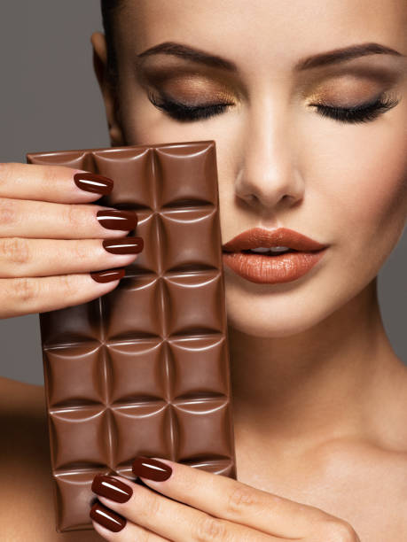 la belle femme avec des ongles bruns retient la barre du chocolat - brown chocolate candy bar close up photos et images de collection