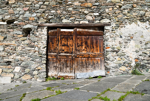Front view of an abandoned stone house with a weathered wood door in the mountain village of Casteldelfino, Varaita Valley, Piedmont, Italy