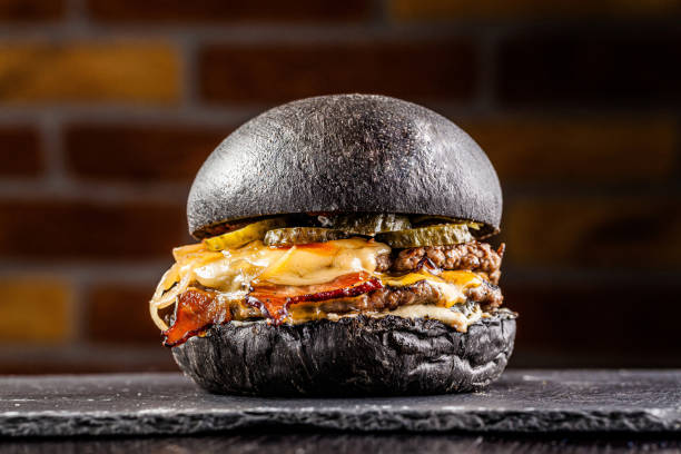american food concept. black bun burger with the words meat and burger, with a meat patty, pickled cucumbers, fried bacon and cheese. copy space - food elegance cutlet restaurant imagens e fotografias de stock