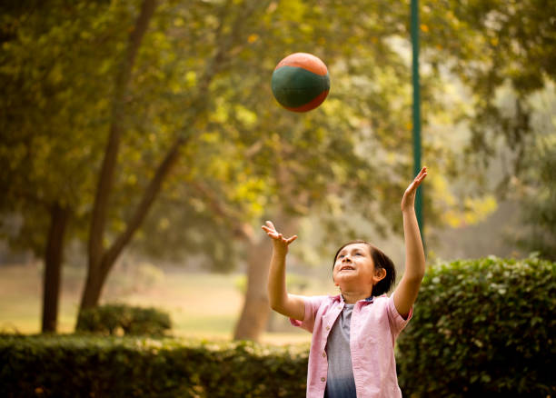 A little Asian girl in a colorful dress holding a red ball or balloon with both hands, on a white background