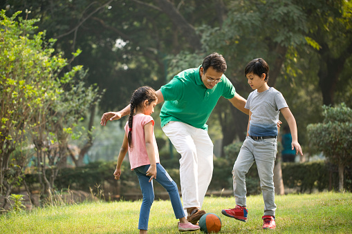 Father and children playing with ball at park