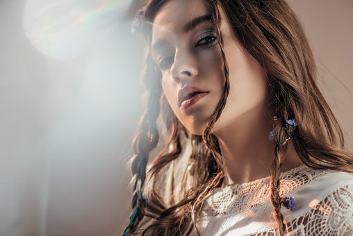 attractive bohemian girl with braids in hairstyle posing in white boho dress on grey with lens flares