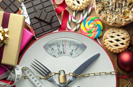 Plate with bathroom scales and padlock surrounded by christmas food and decorations