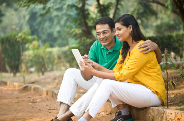 istock Happy Indian couple watching media content using digital tablet at park 1193920957