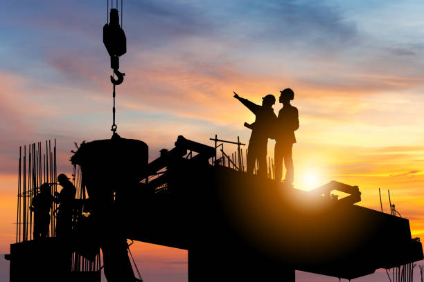 Silhouette of Engineer and worker checking project at building site background, construction site at sunset in evening time.