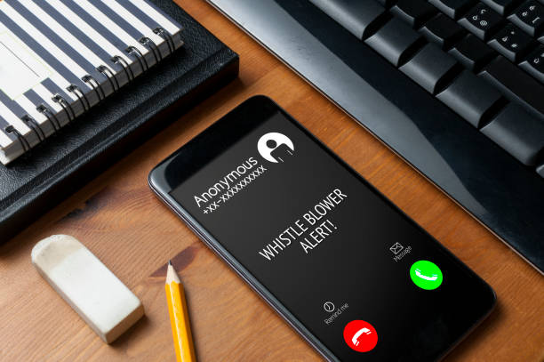 istock Whistleblowing concept: smartphone on wooden table show a whistle blower alert on an anonymous call 1193926869