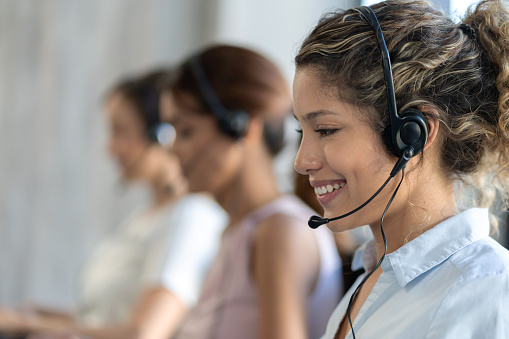 Happy operator working at a customer service call center using a headset  - focus on foreground
