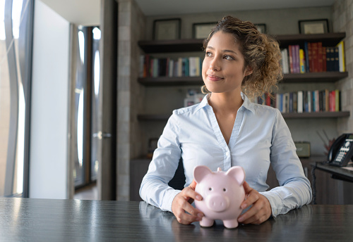 Business woman thinking how to spend her savings while holding a piggybank