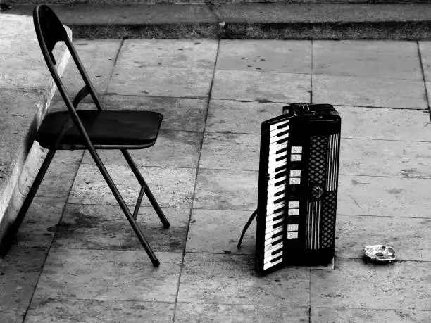 Abstract urban scene in monochrome. street musician`s empty stand with accordion and empty chair. stone pavement and coin tray for money collection. lifestyle and urban living concept.