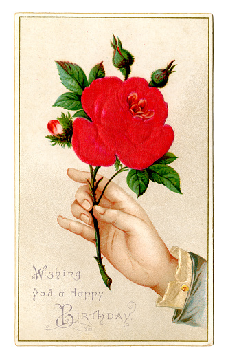 A Victorian birthday card with an embossed illustration of a large bright red rose being held by a rather small hand and the message “Wishing you a Happy Birthday”.