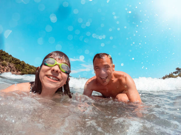 istock Father and daughter getting splashed by the sea wave 1193946887
