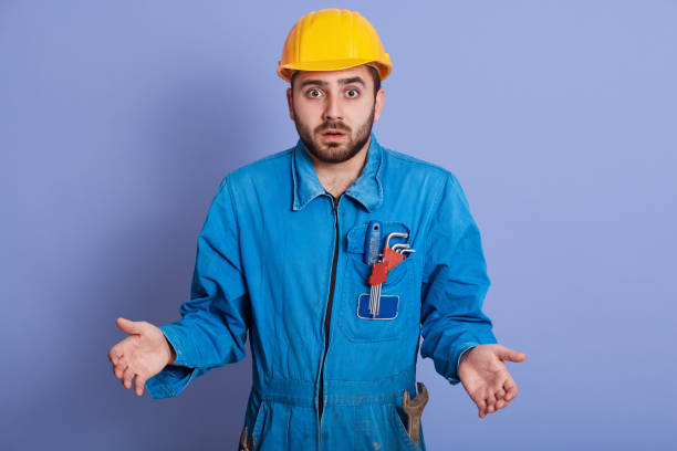 istock Astonished shocked young builder wearing yellow helmet and blue uniform, standing with opened mouth and spreading hands, making helpless gesture, handsome guy looks surprised. People emotions concept. 1193956434