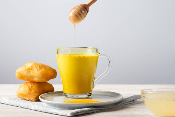 Golden milk with turmeric and honey, a traditional Indian drink on a white wooden background stock photo