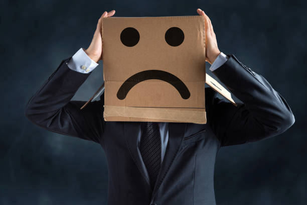 Businessman with drawn sad face on cardboard box over his head