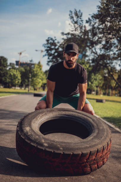 istock Bearded man with hat flipping tire in the park 1193964409