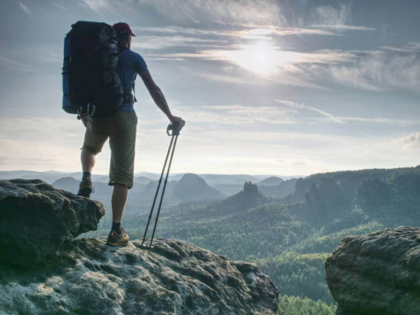 Guy hold sticks in one hand. Hiker stop for watching landscape from sharp sandstone summit.