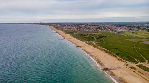 An aerial view of a sandy beach with groynes (breakwaters), crystal blue water, dunes, grassy field and city in the background under a grey sky An aerial view of a sandy beach with groynes (breakwaters), crystal blue water, dunes, grassy field and city in the background under a grey sky hengistbury head photos stock pictures, royalty-free photos & images