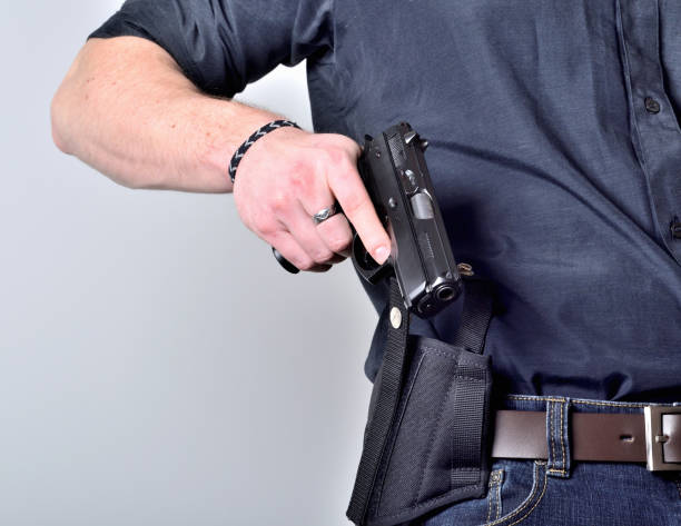 plan rapproché de la main de l'homme tirant dehors un pistolet de pistolet de l'étui sur la ceinture, jeans, chemise noire - handgun gun blue black photos et images de collection