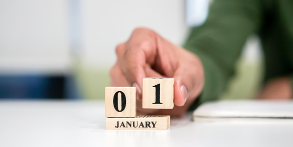 close up employee man hand put number 1 of cube shape wood to make calendar date January at office desk for the new day in first date of the year countdown concept