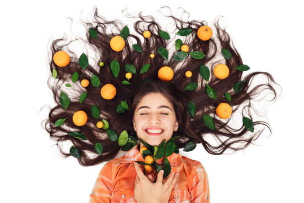 young beautiful cheerful girl lies on floor with her loose hair in mandarins and calamondins. isolated on white. natural skin and hair care products concept. young beautiful cheerful girl lies on floor with her loose hair in mandarins and calamondins. isolated on white. natural skin and hair care products concept oranges with faces stock pictures, royalty-free photos & images