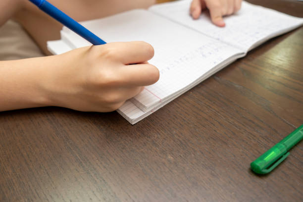 istock A schoolboy doing homework, he is writing in a notebook with a pen, hands close up 1193992039
