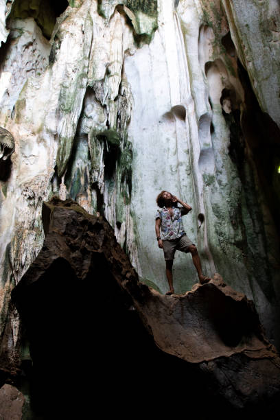 One male tourist, visiting hidden caves in Kampot, Cambodia One young man, wearing shorts and a light shirt, looking to the roof of a big cave located in Kampot, Cambodia. kampot stock pictures, royalty-free photos & images